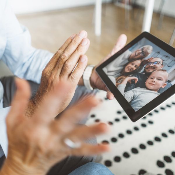 Grandparents talking to their family and grandchildren over a video call. Senior couple sitting on the couch in the living room, talking to family over video call on digital tablet.