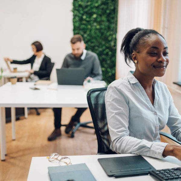 Successful smiling african american businesswoman using a laptop while working on a new project at the office. Bright modern work station. Analyzing market stock, creating a new business strategy.