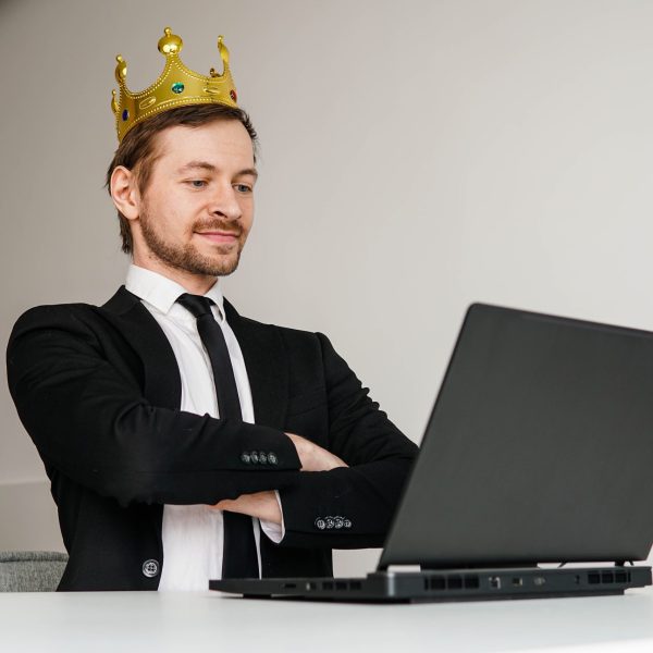 Self-confident arrogant businessman with golden crown on head using laptop.